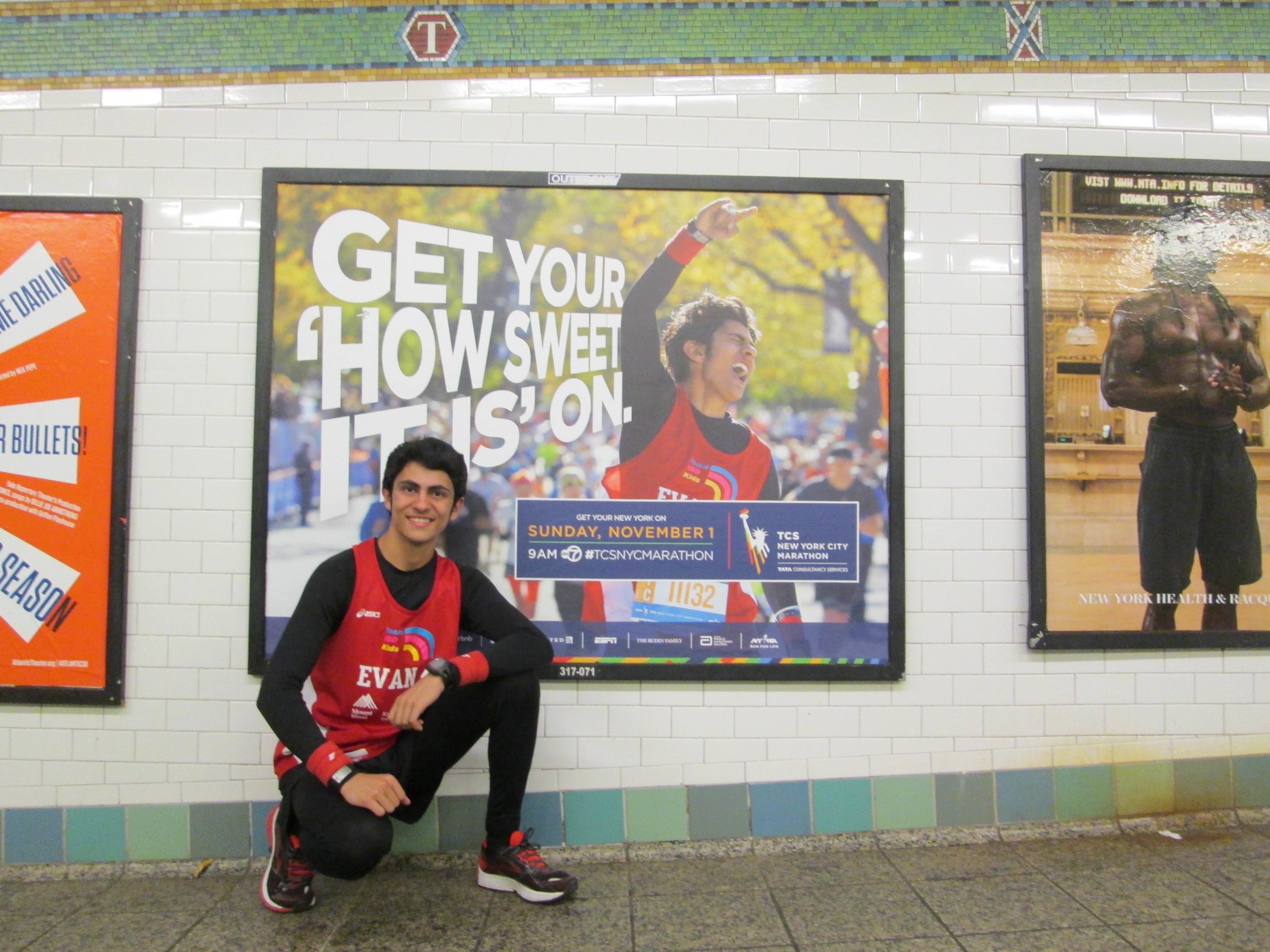 Evan in front of a New York Road Runners subway advertisement for the NYC Marathon