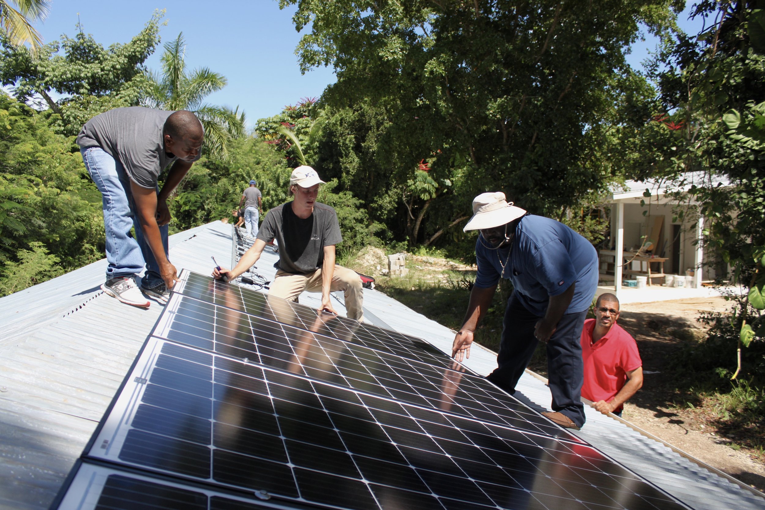 Michael, one of our general systems interns and two participants work to install the solar modules along the roof.